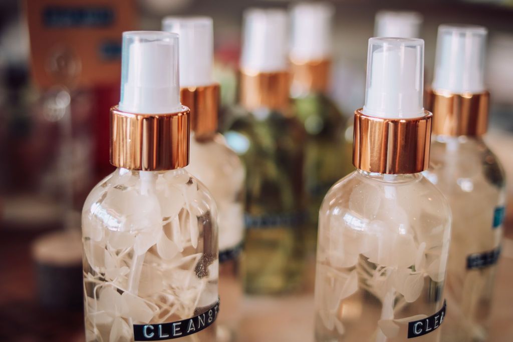 Clear spray bottles with copper-colored collars, filled with flowers, on a wooden surface.