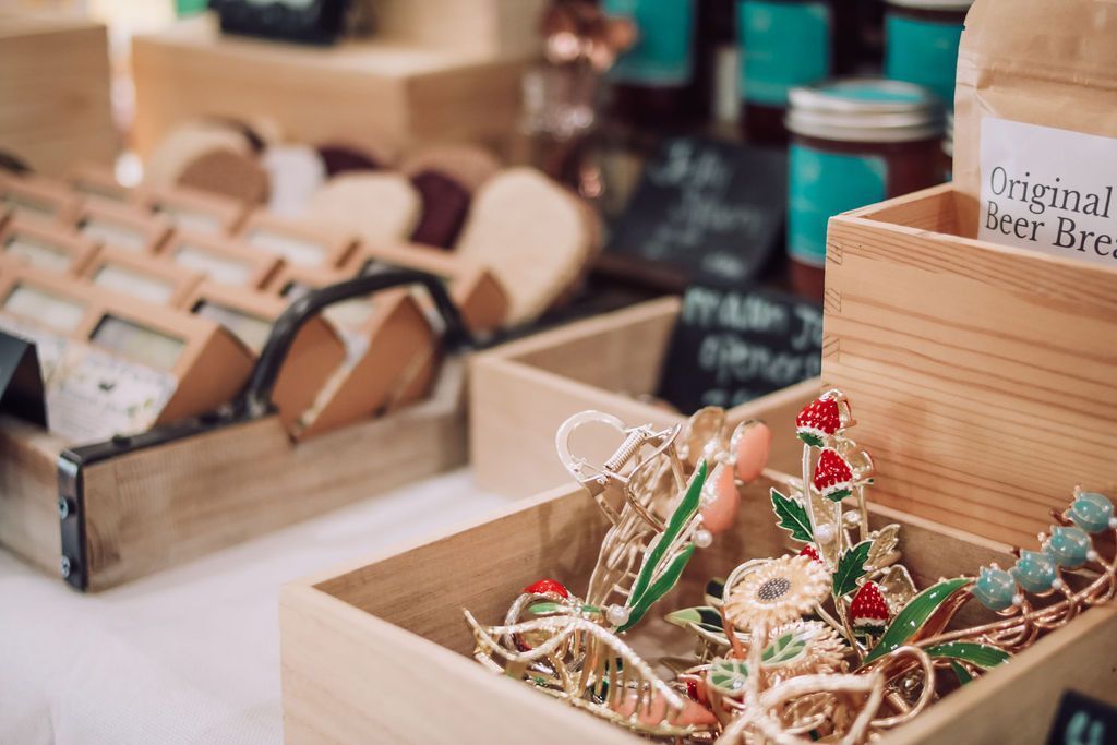 Wooden display boxes holding handmade jewelry and other goods at a market.