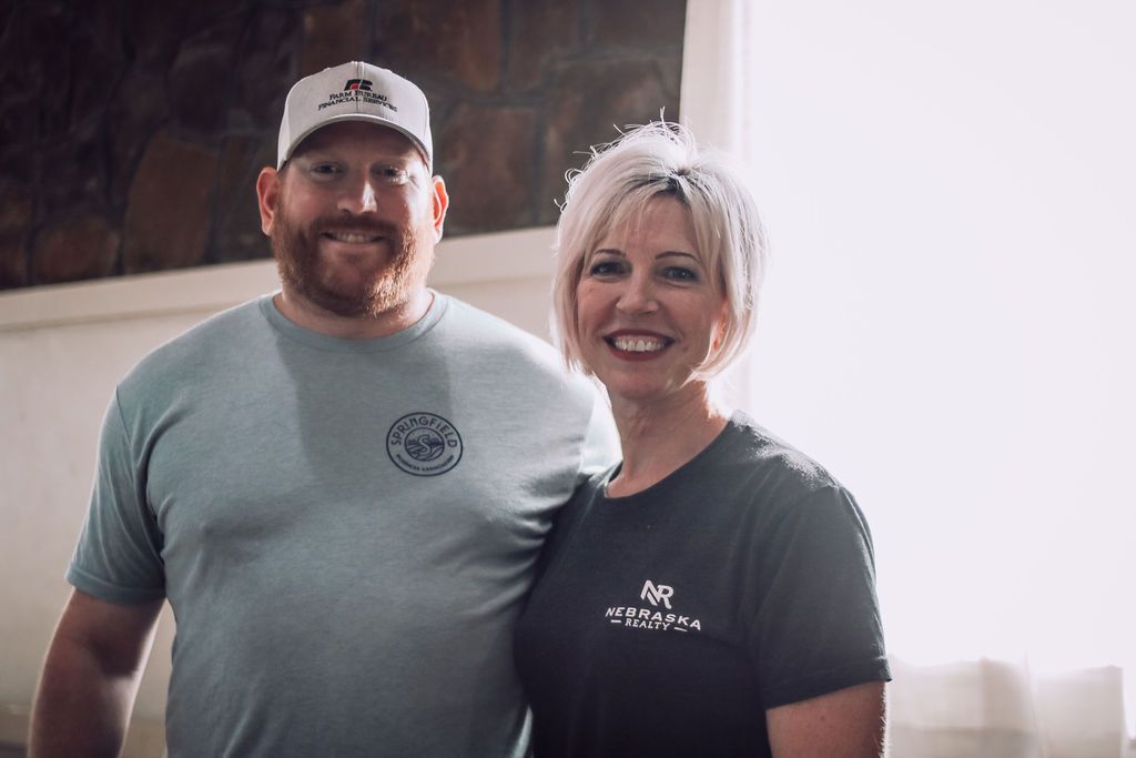 Man and woman smiling, indoors. Man wears a hat and t-shirt; woman wears a t-shirt.