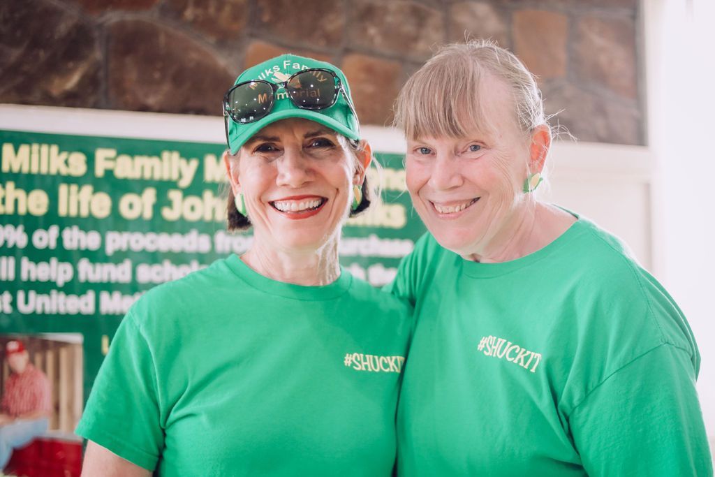 Two smiling women in green shirts, standing together in front of a sign.