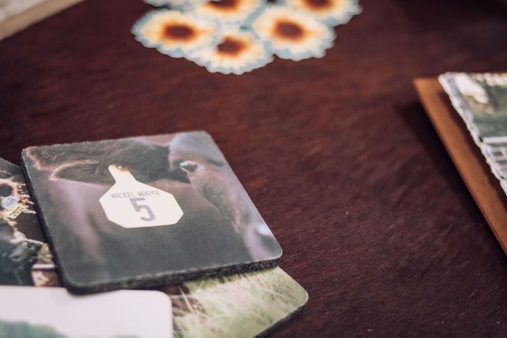 Cow-themed coaster with number 5 on tag, blurred floral design, on a brown textured surface.