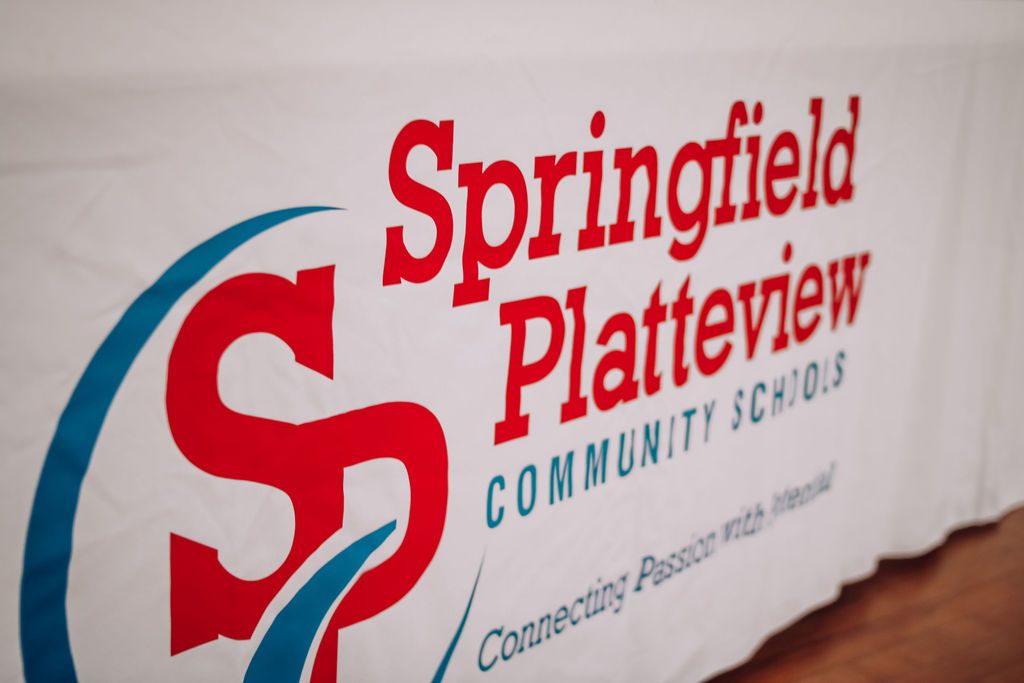 Springfield Platteview Community Schools logo on white banner. Red letters over blue graphic.