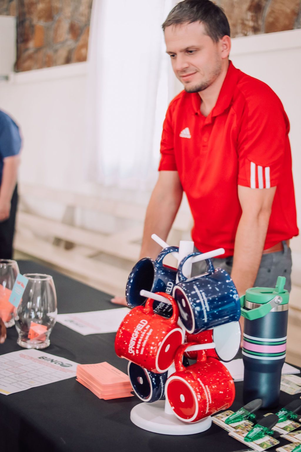 Man in red shirt stands behind a table with mugs on a display stand.