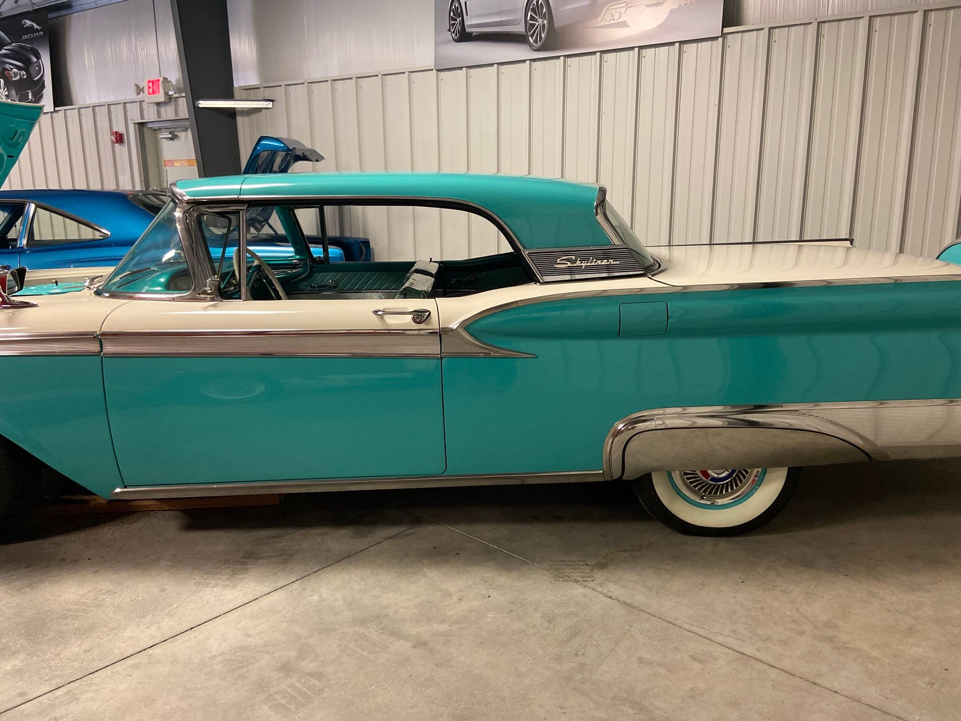 Turquoise and white vintage car with chrome trim, parked indoors.