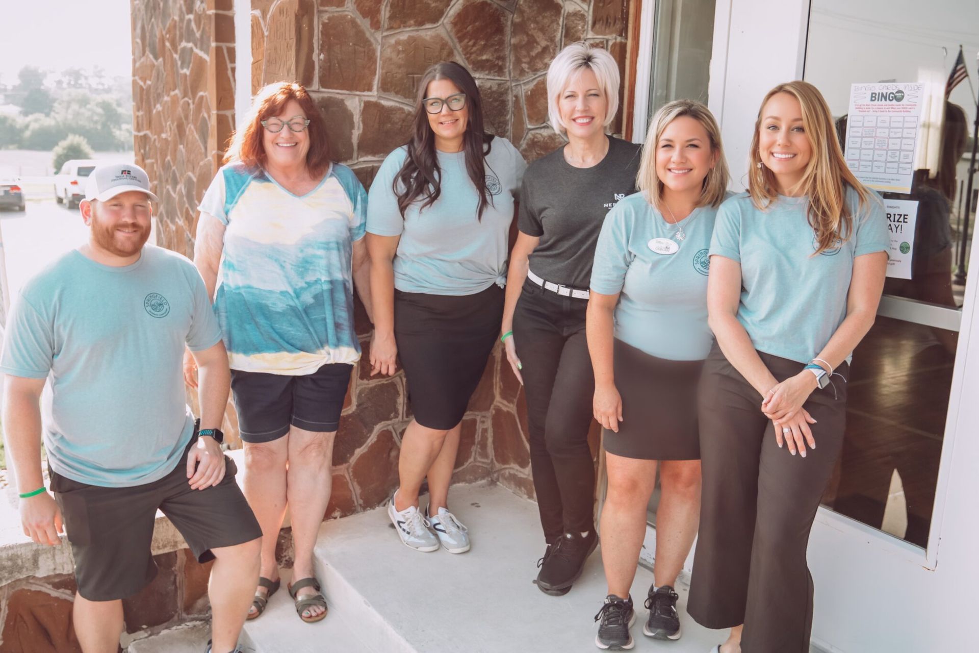 Group of people in matching teal shirts posing outside a building.
