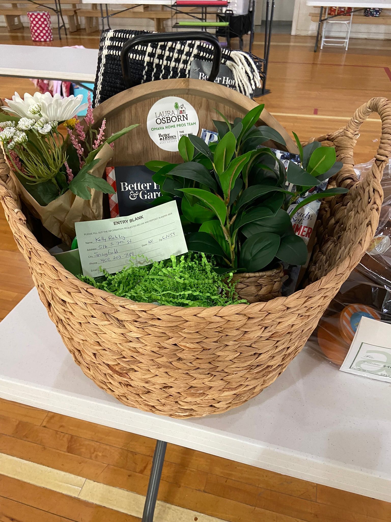 A large woven basket filled with plants and gift items on a table.