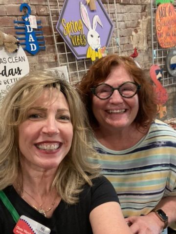 Two smiling women pose in front of spring-themed decorations.