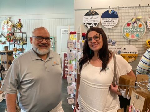 Two people standing in a craft store smiling, surrounded by handmade decor and products.
