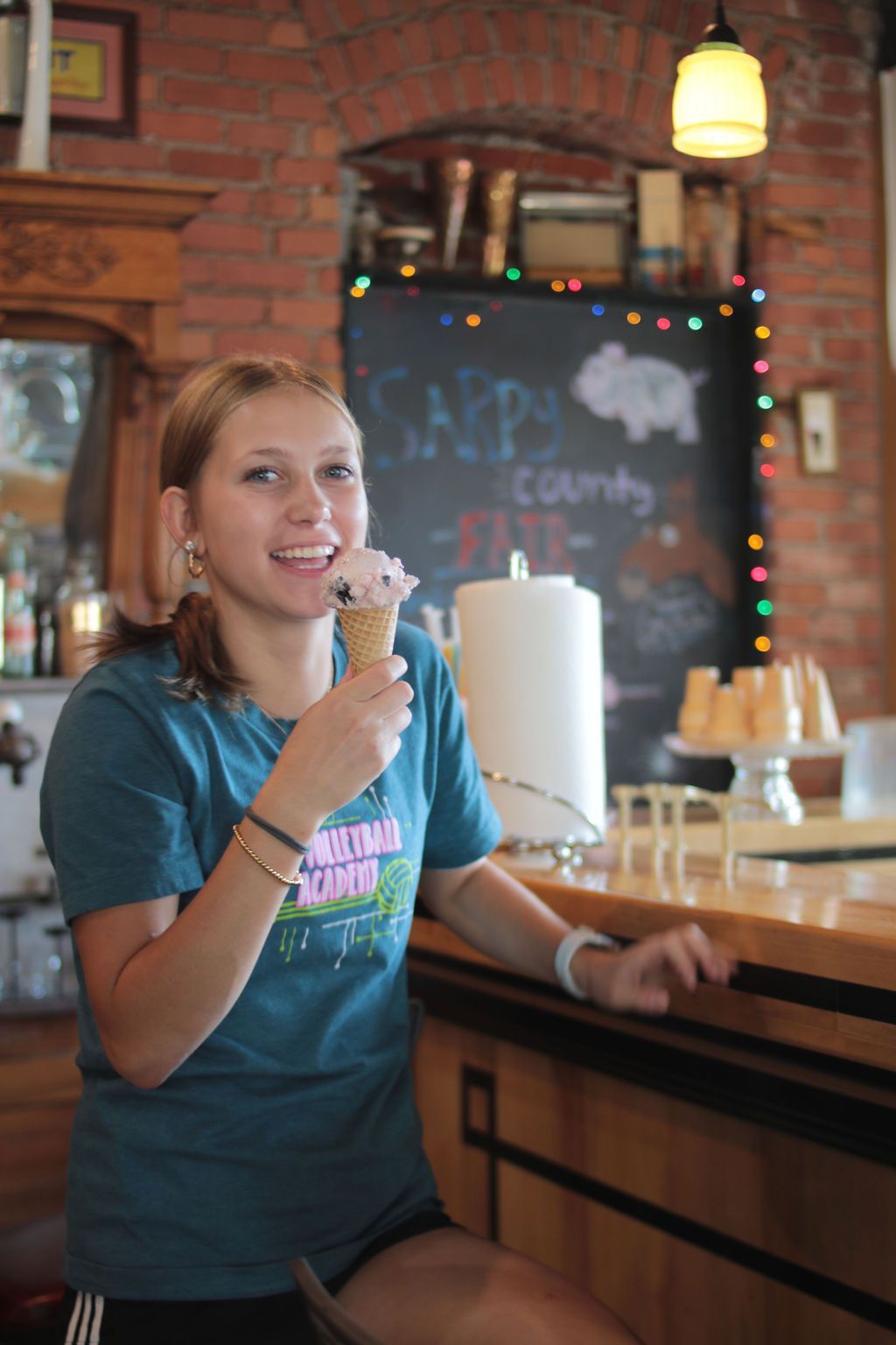 Woman smiling, eating ice cream cone at a counter in a brick-walled ice cream shop.