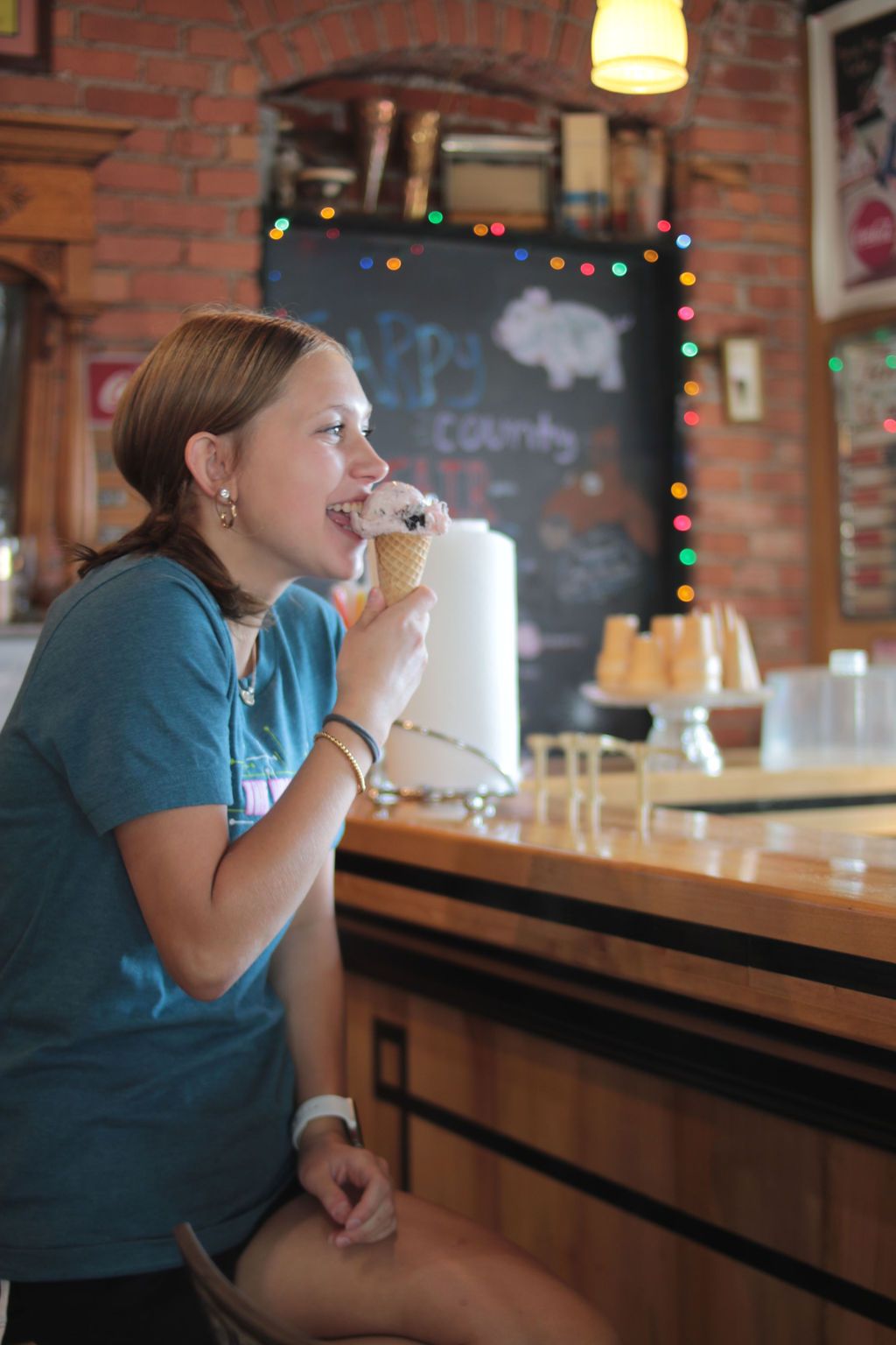 Woman eating ice cream at a counter in a brick-walled shop.
