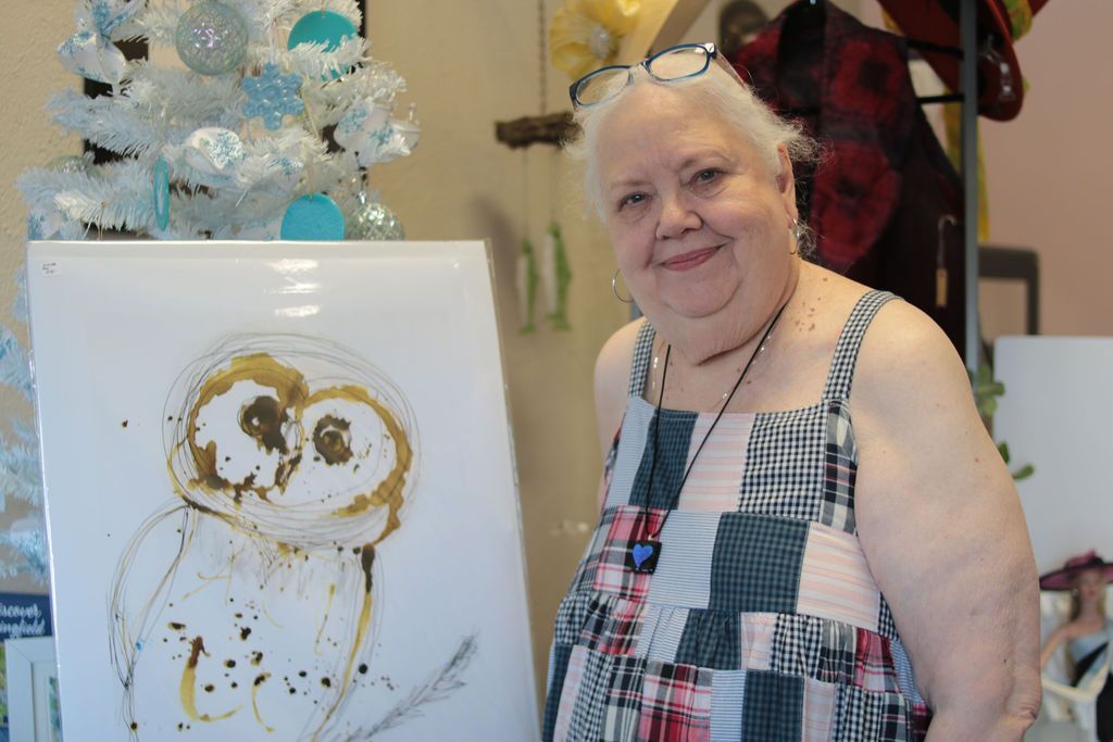 Woman with glasses smiles next to an owl painting and a white Christmas tree.