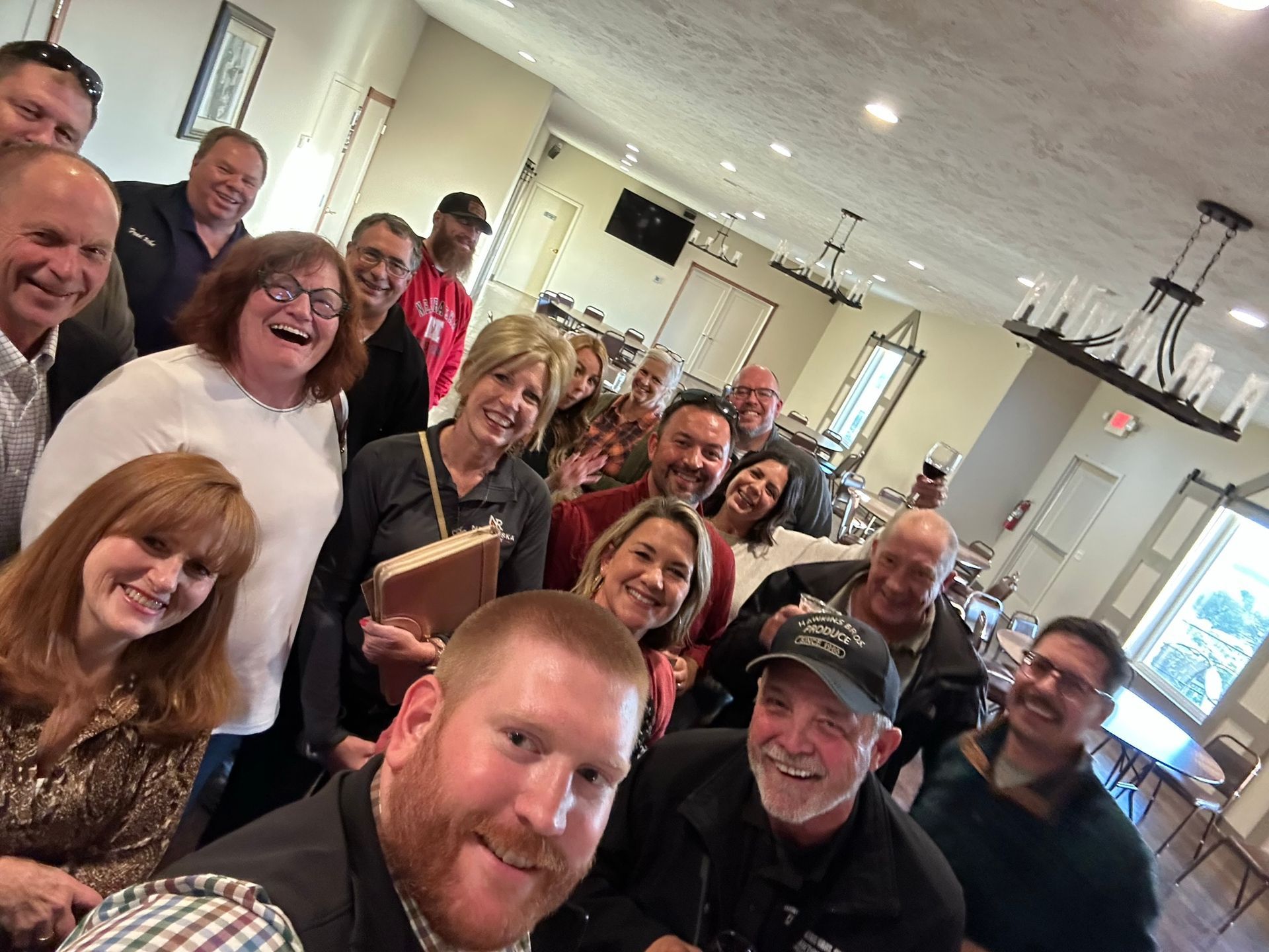 Group of people smiling for a selfie in a brightly lit room with a chandelier.