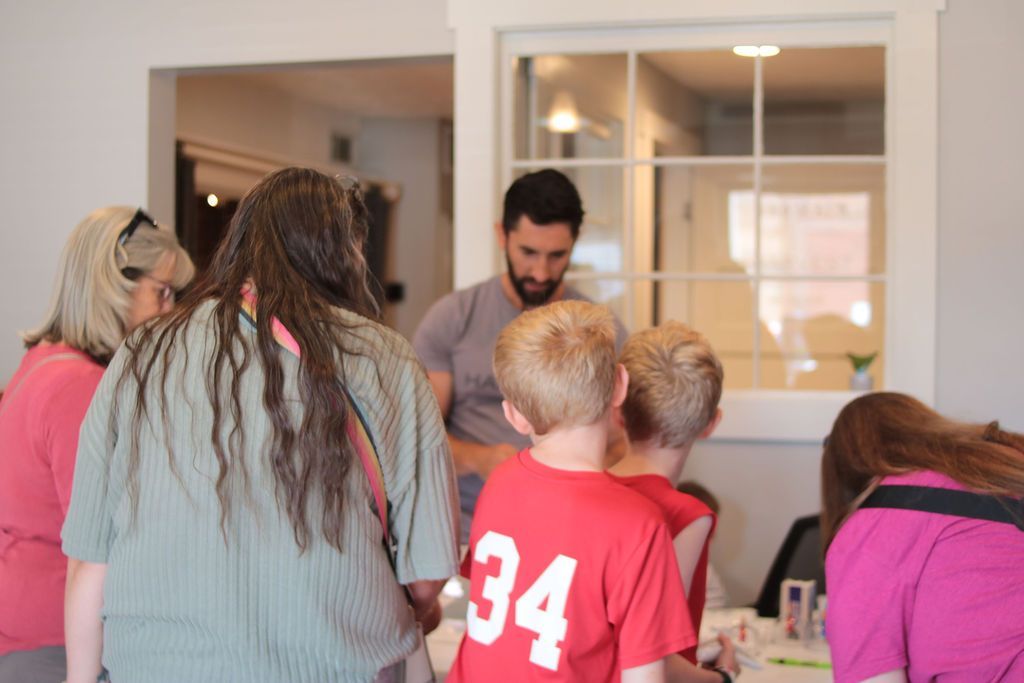 People gathered indoors, observing a man examining two boys. The boy in red shirt shows 