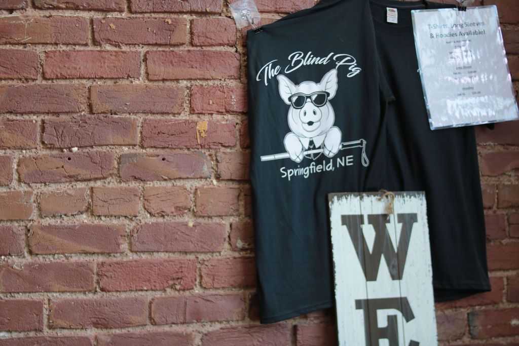 Brick wall with a black t-shirt featuring a pig logo, a welcome sign, and a printed menu.