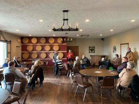 People gathered in a room with wine barrels on the wall. A speaker stands in the center.