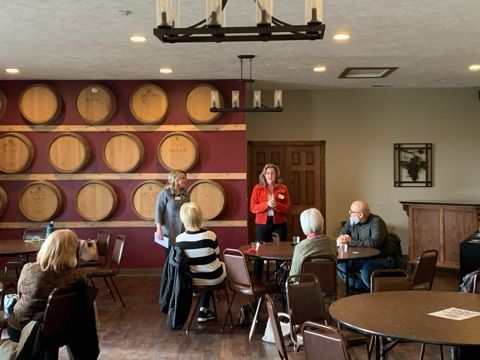People at tables in a room, two women speaking near a wine barrel display.