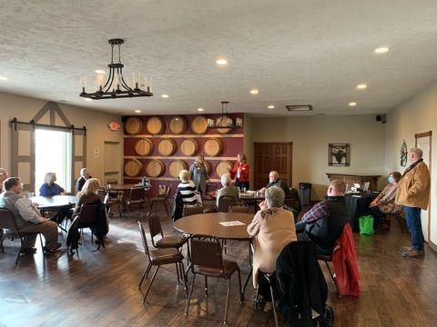 Group of people in a room with a wall of barrels. Some sit, others stand talking.