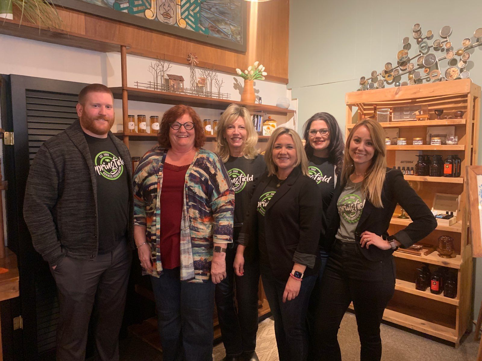 Group of people posing together inside a shop, smiling. Shelves with products, art on the wall.