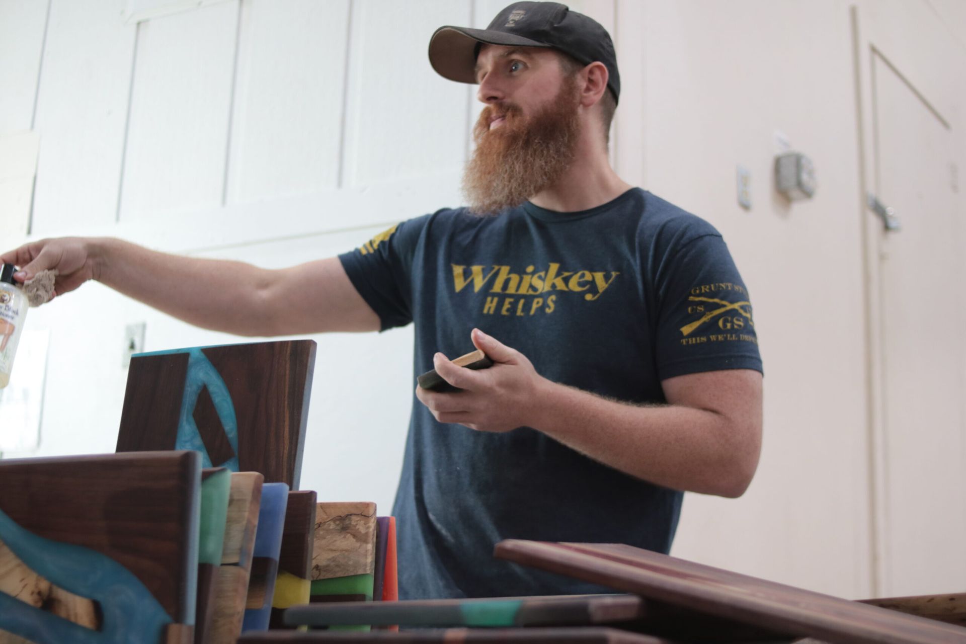 Man with beard in workshop, pointing. He wears a hat and 