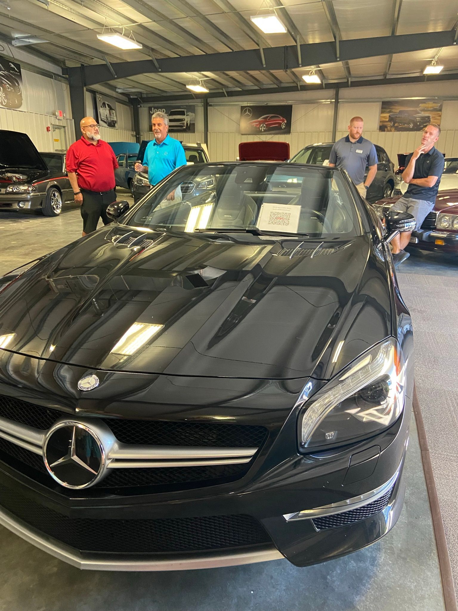 Black Mercedes convertible in a showroom with four men standing nearby.