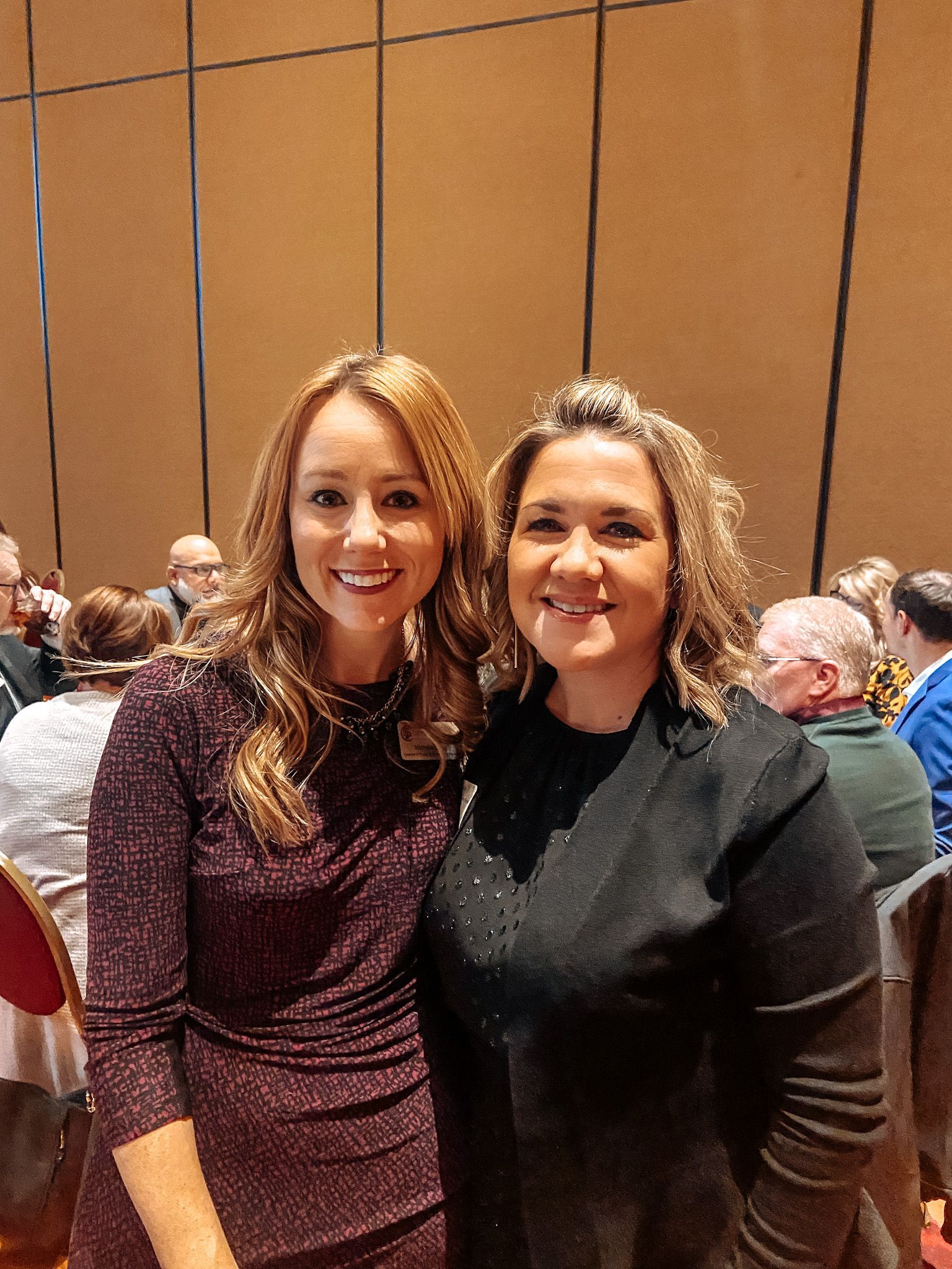 Two smiling women pose together at an event. One in a sparkly burgundy dress, the other in a black top.