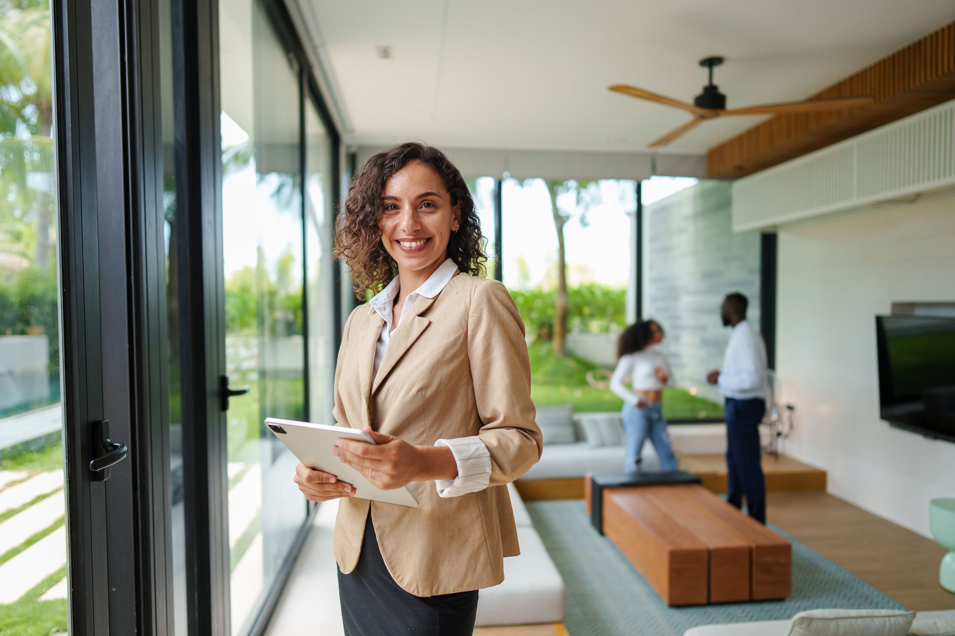 Smiling professional holding a tablet in a modern living room with two people in the background
