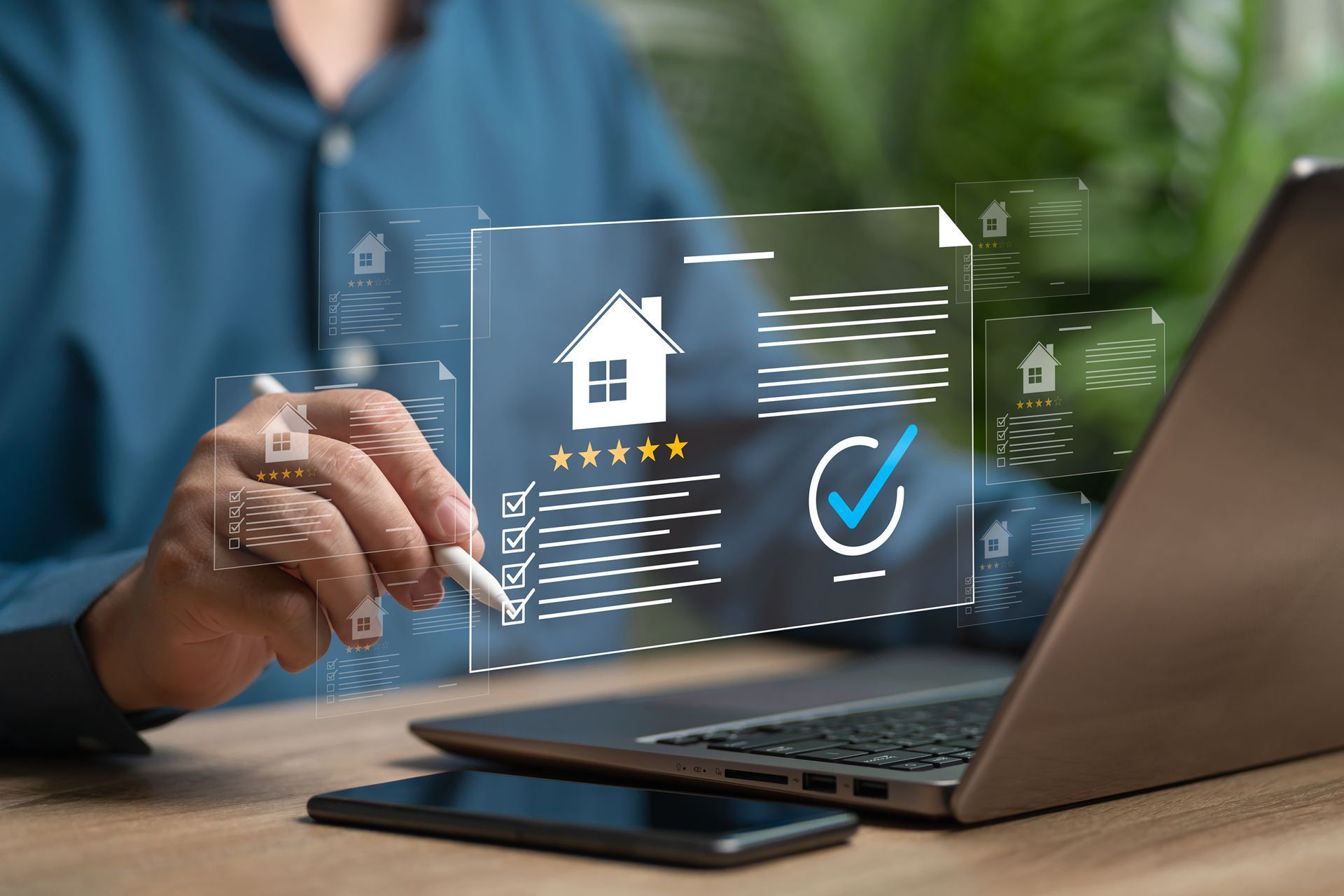 Hand using tablet beside laptop with virtual house icon and checkmark, suggesting online home purchase or approval
