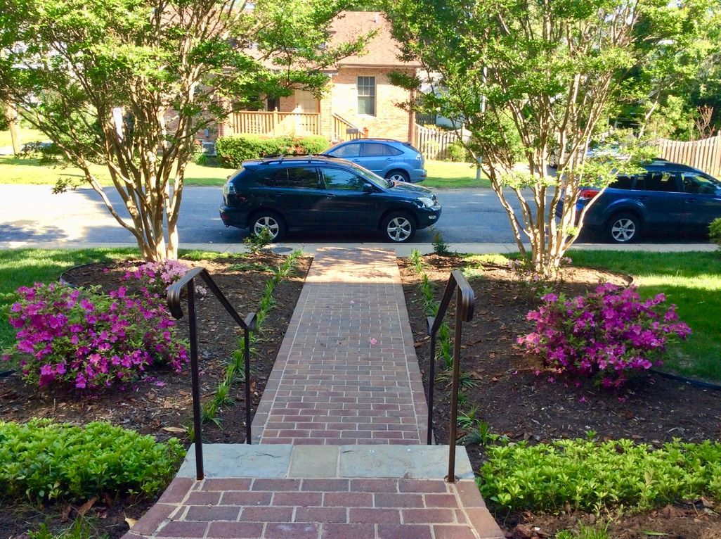 A car is parked on the side of the road next to a brick walkway.