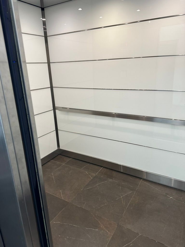 The inside of an elevator with white walls and a brown tile floor.