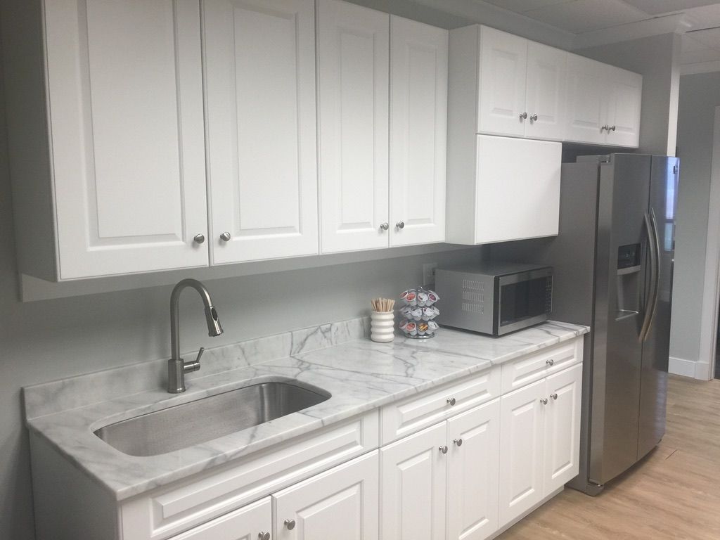 A kitchen with white cabinets , a sink , a refrigerator , and a microwave.