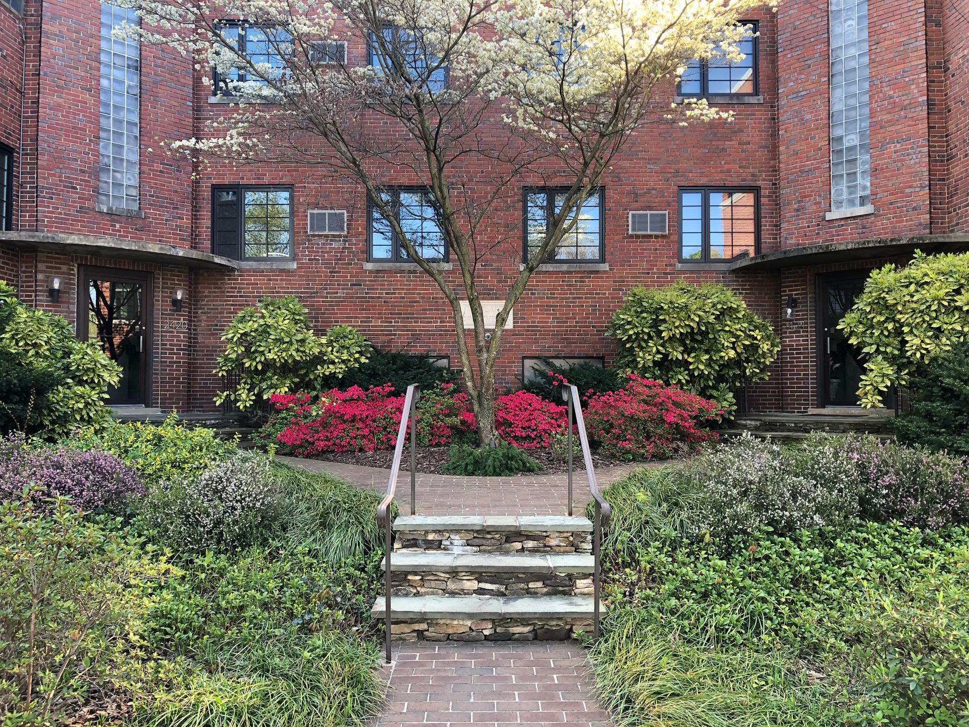 A brick walkway leading to a brick building surrounded by trees and bushes.