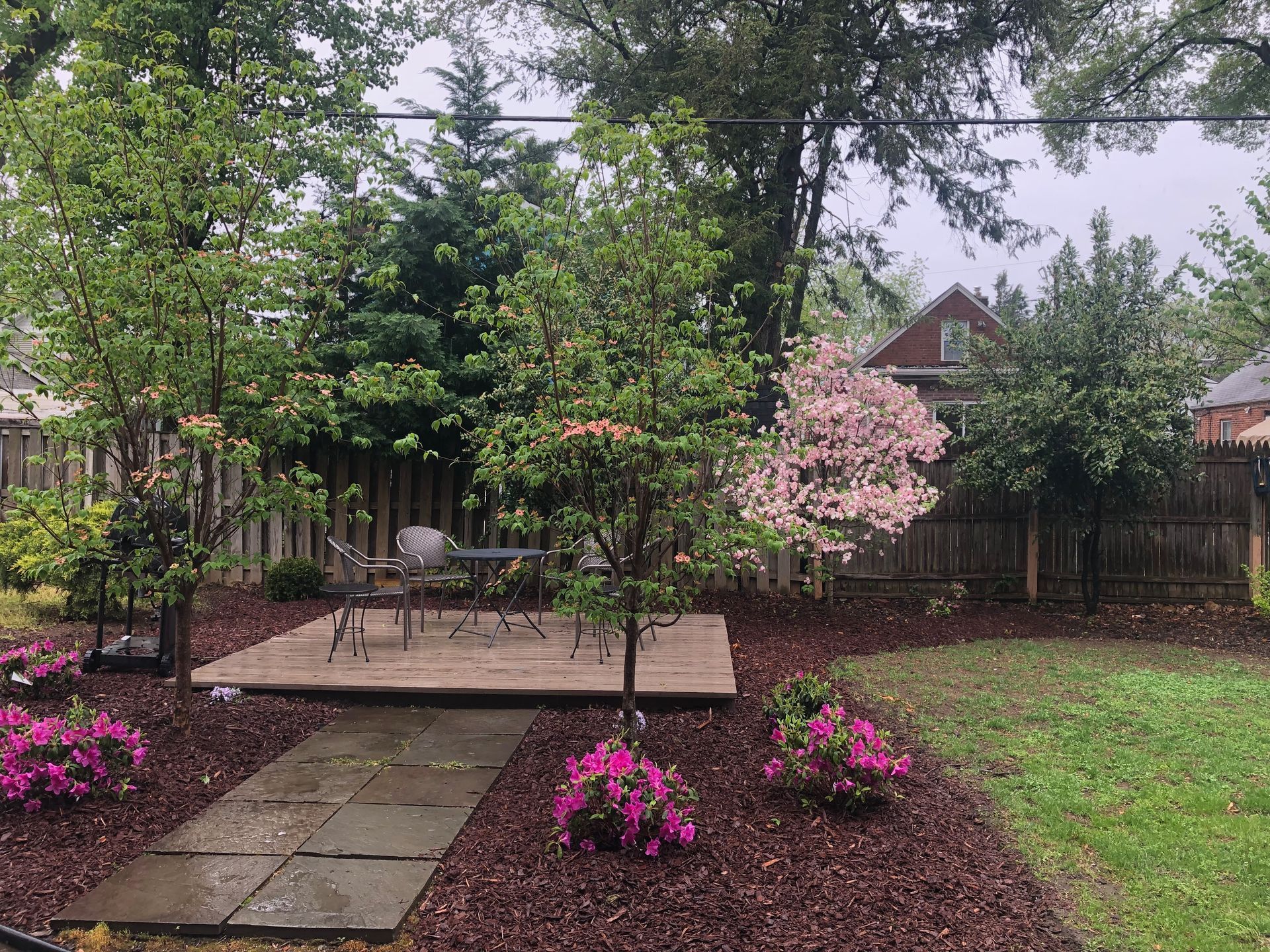 A backyard with a table and chairs and flowers on a rainy day.