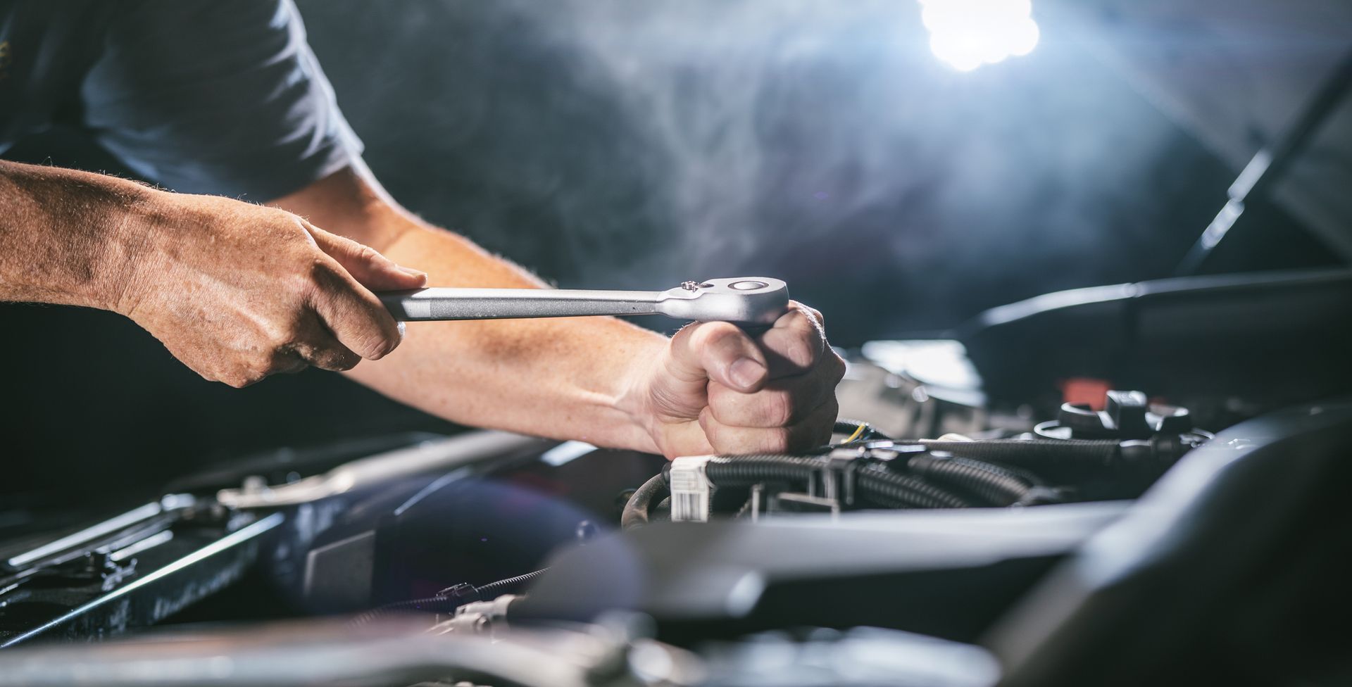 A man is working on a car engine with a wrench.