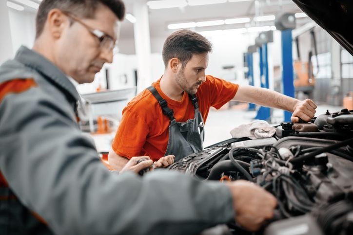 Two mechanics are working on a car engine in a garage.