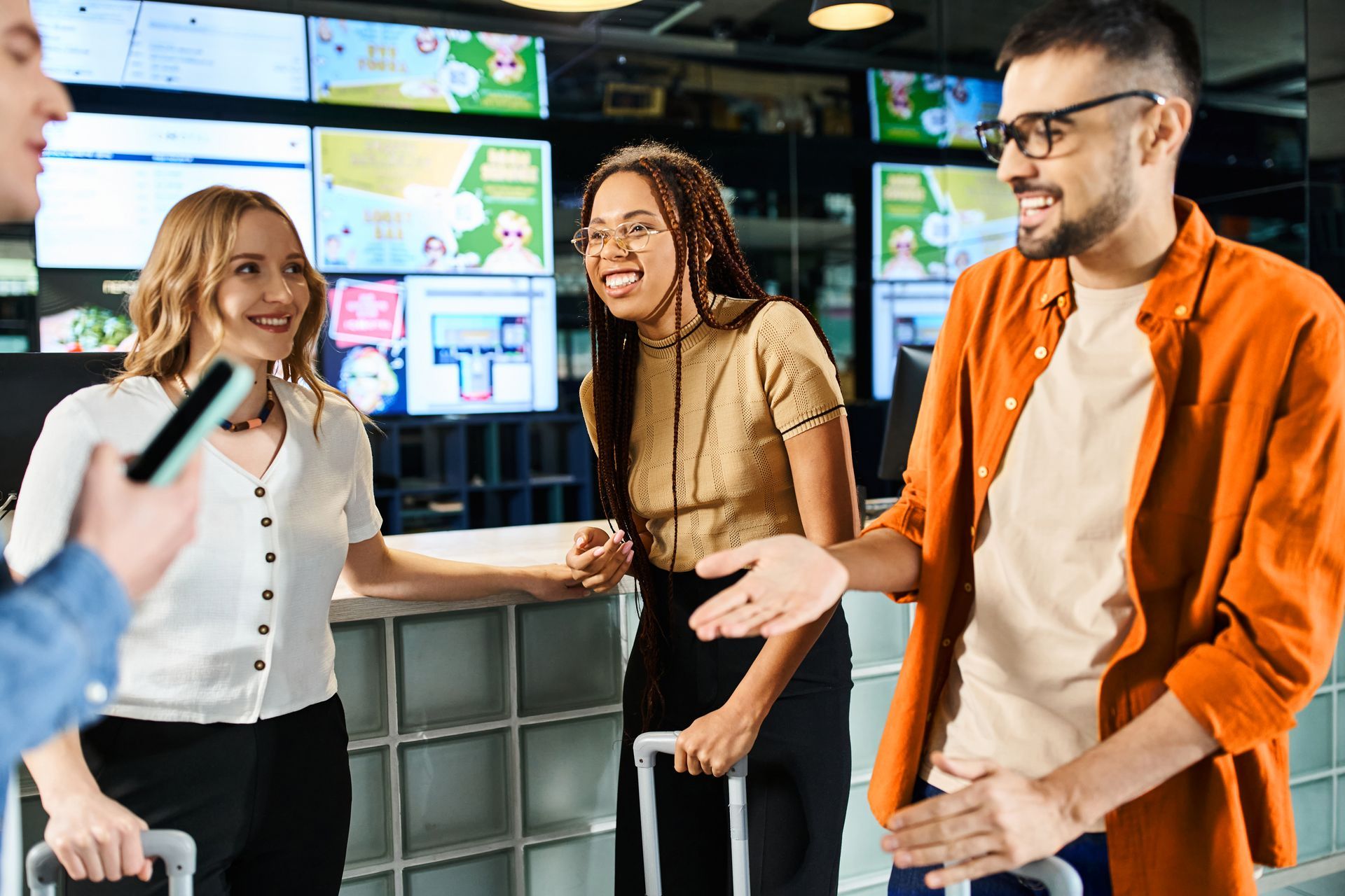 Three coworkers chatting in a bright office with wall screens, smiling and gesturing