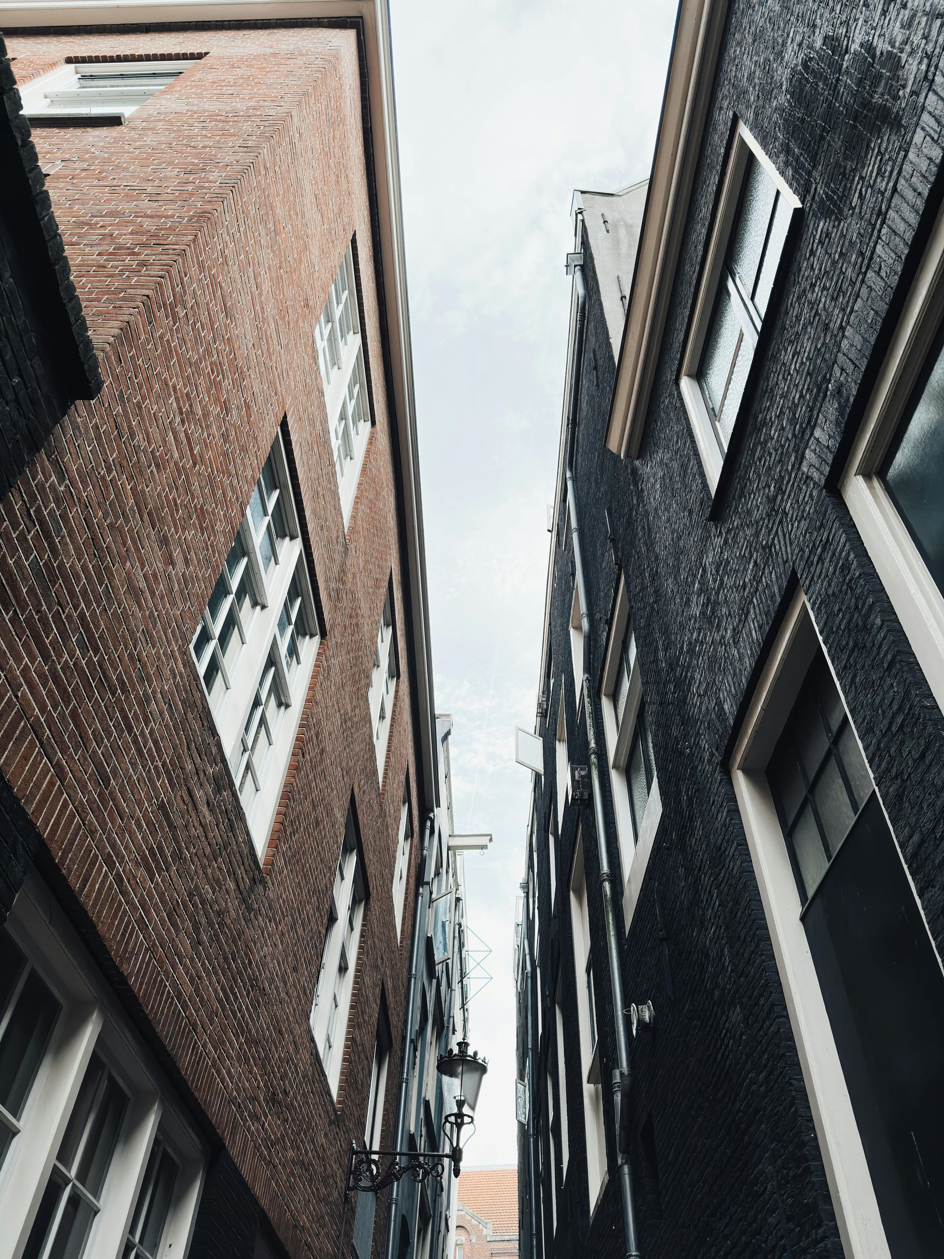 Hoge bakstenen gebouwen in een smalle steeg, met daarboven een heldere, bewolkte hemel.