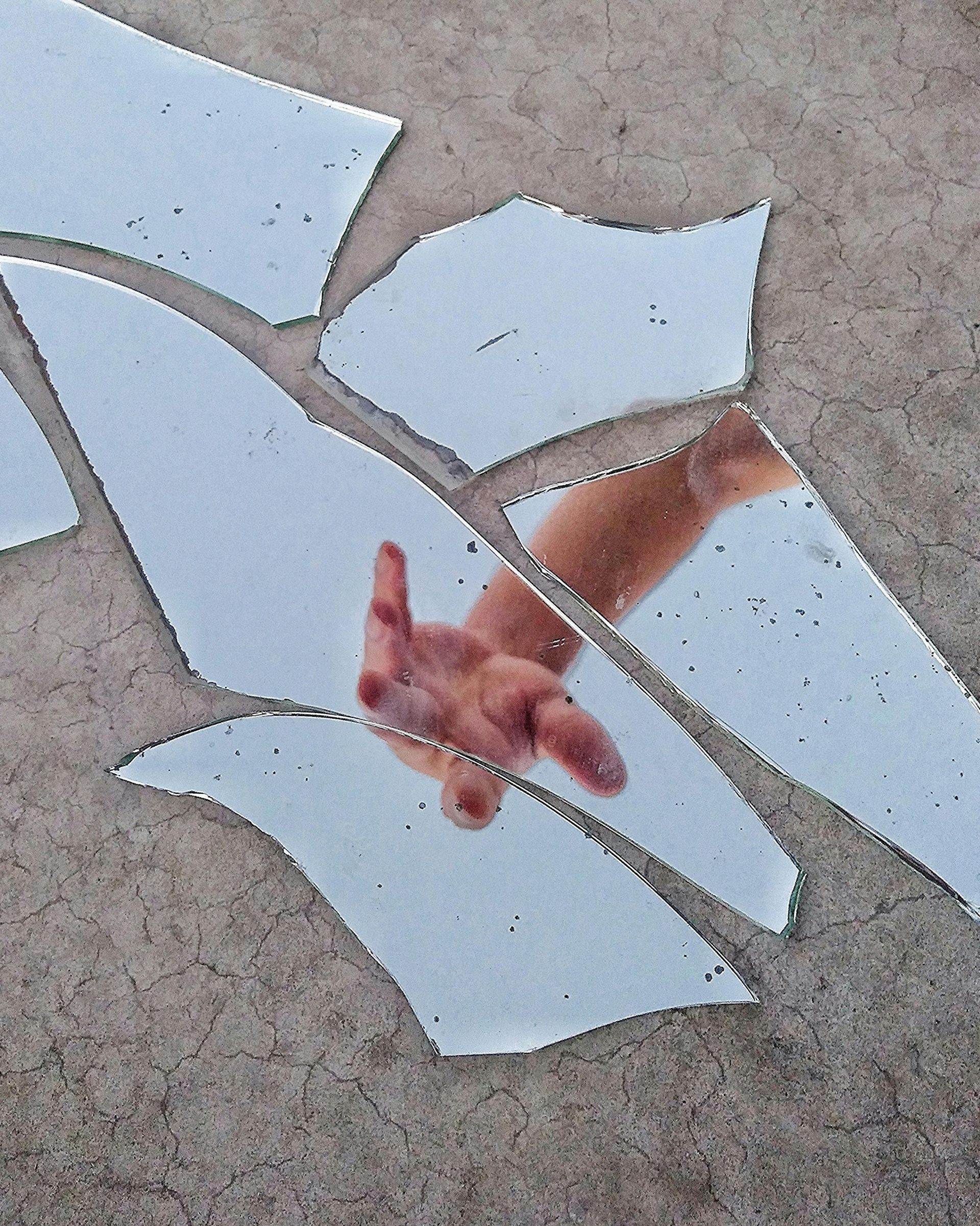 Gebroken spiegelstukjes op beton weerspiegelen een hand en onderarm die ernaar reiken.
