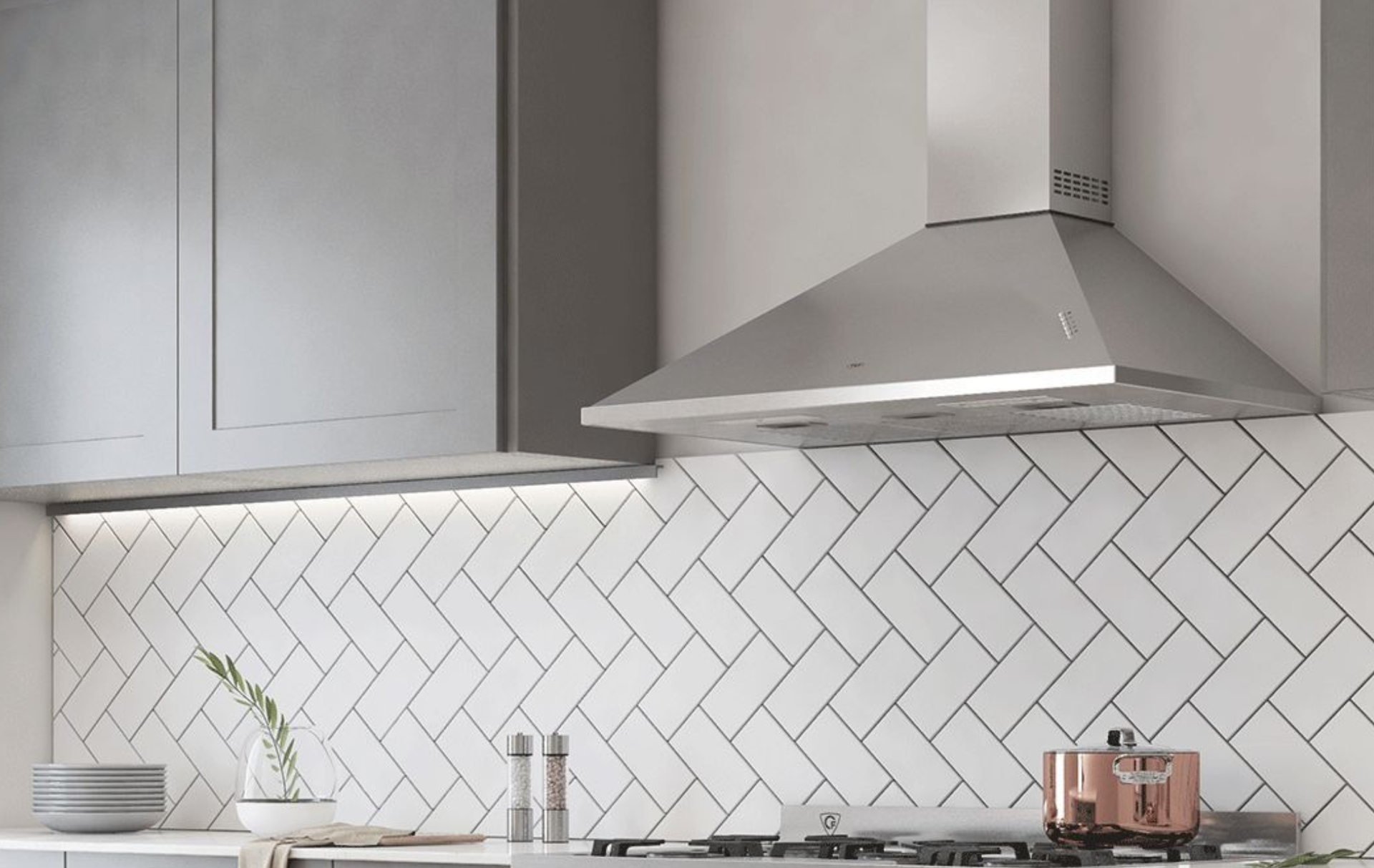 Cocina moderna con gabinetes grises, salpicadero de azulejos blancos en espiga y campana extractora de acero inoxidable.