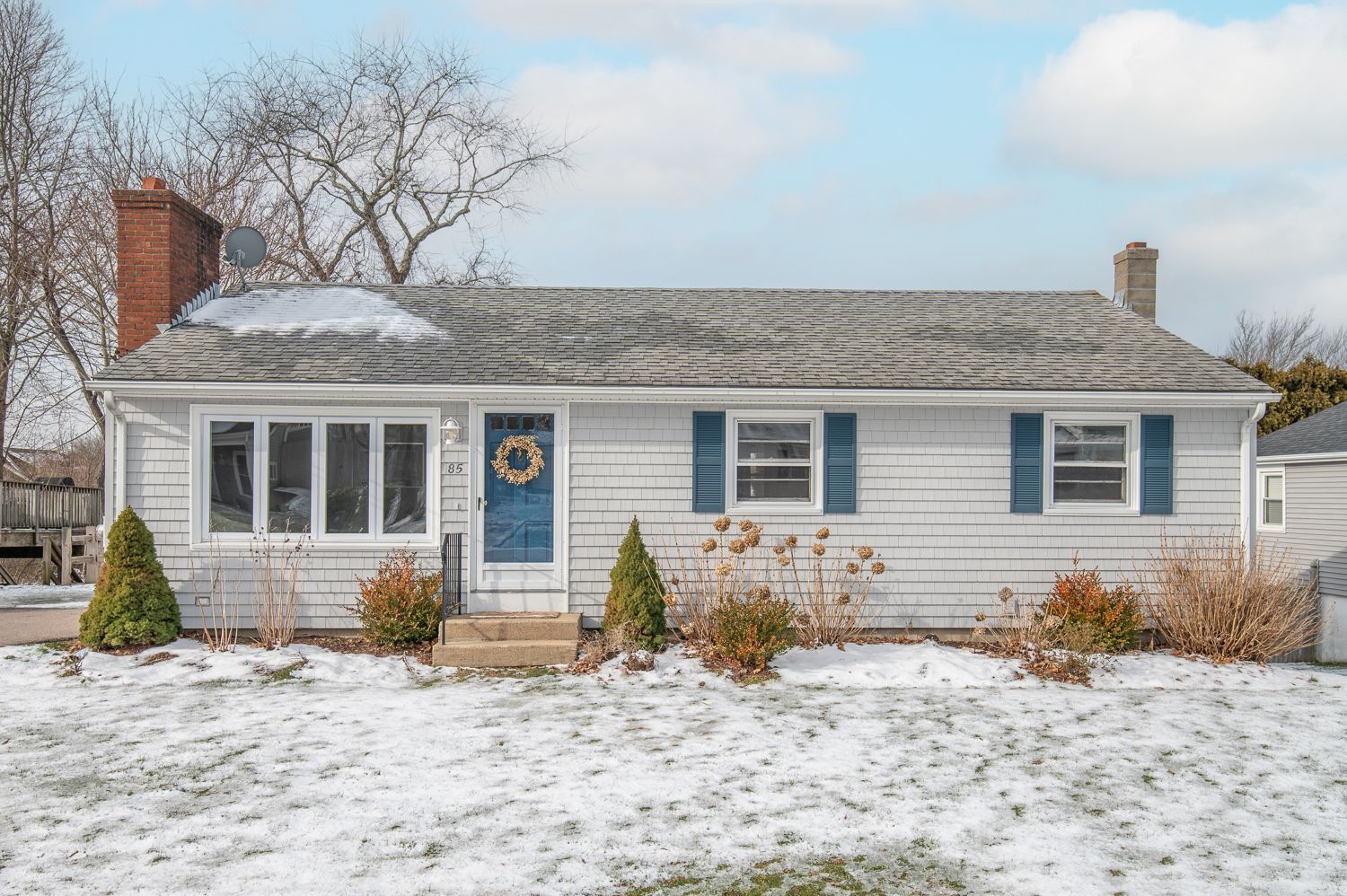 A white house with blue shutters and a blue door is surrounded by snow.