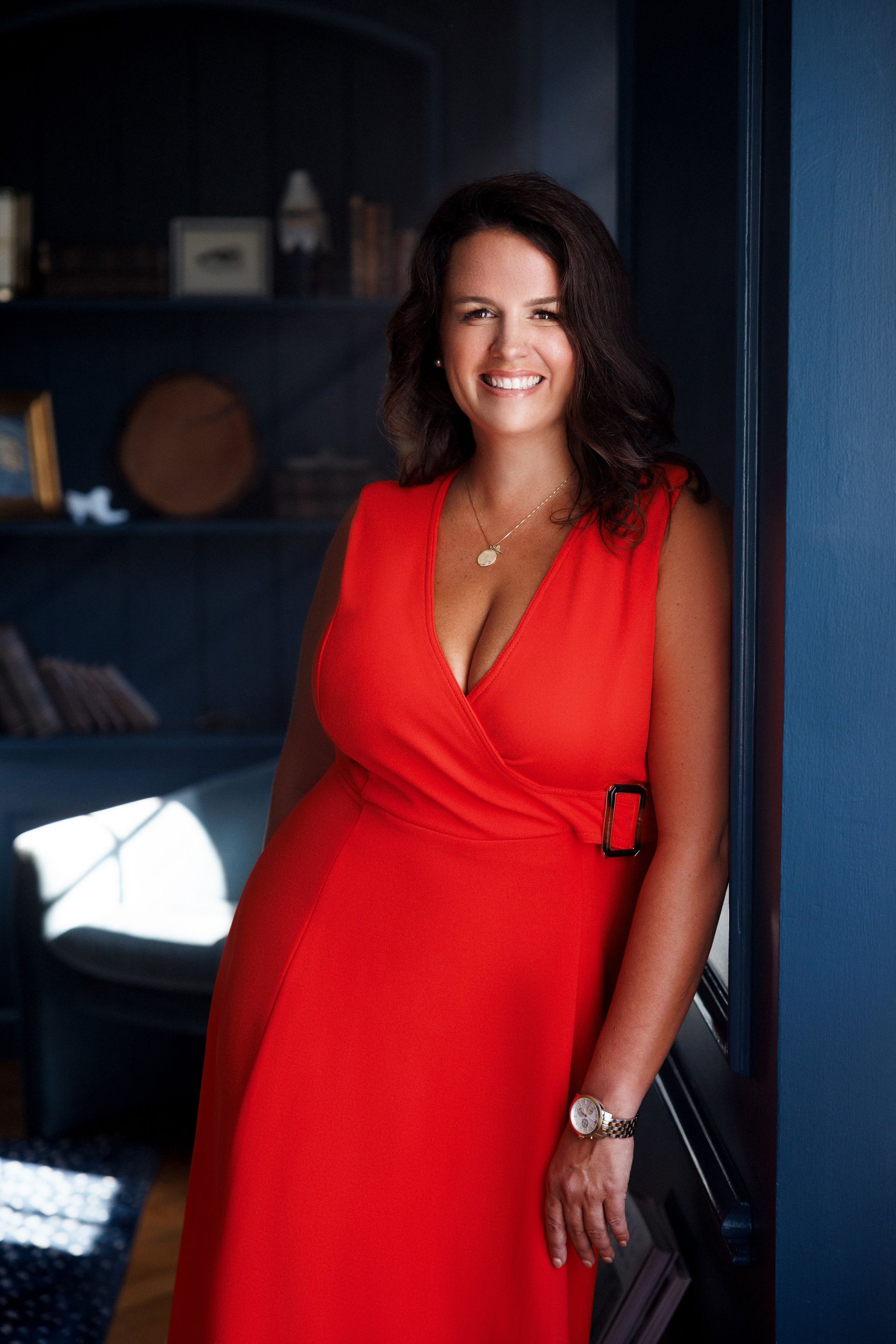 A woman in a red dress is standing next to a blue wall.