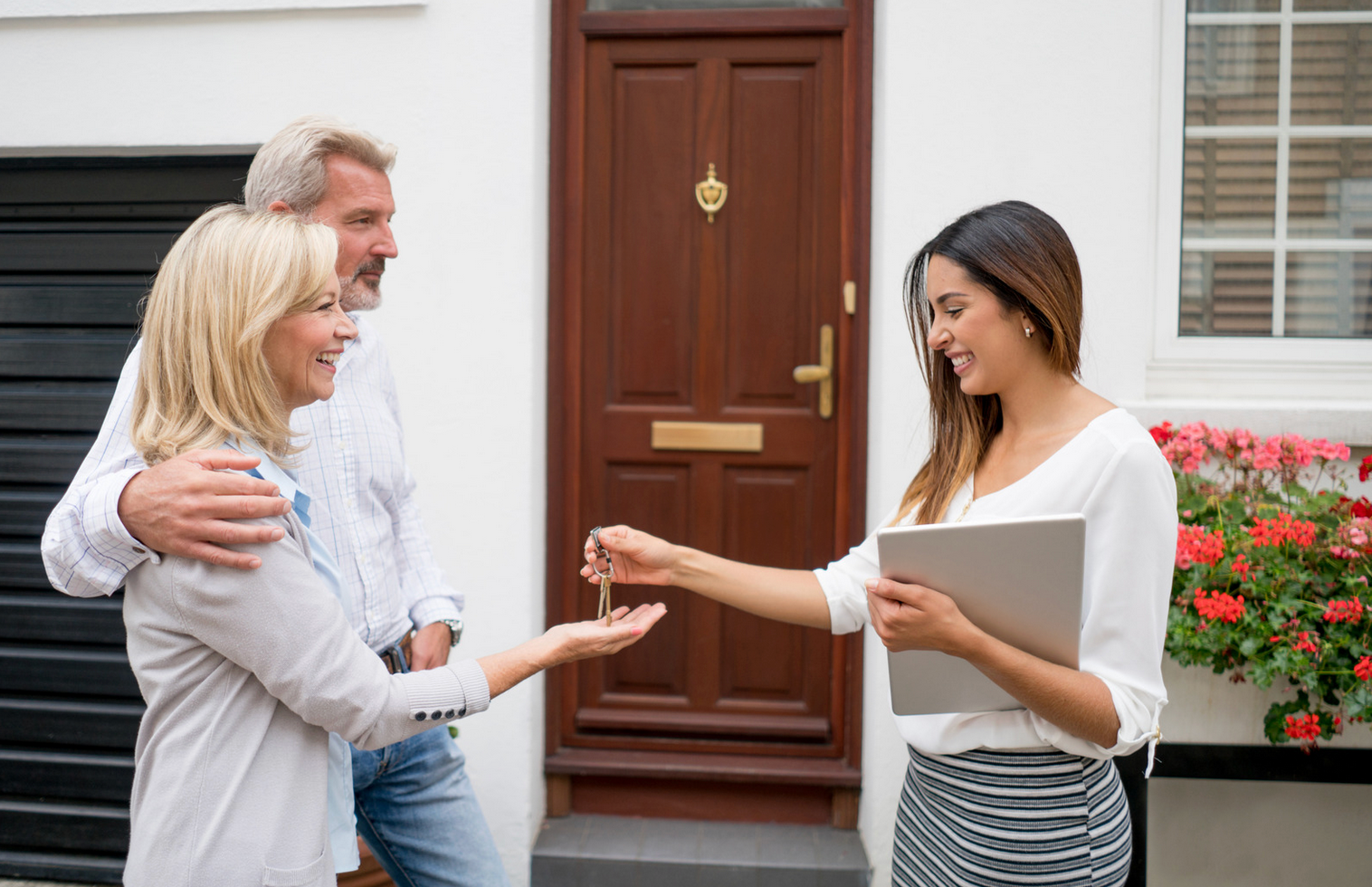 A woman is giving a man and woman keys to their new home.