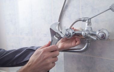 Hands using a wrench to adjust a bathroom shower faucet against tiled wall