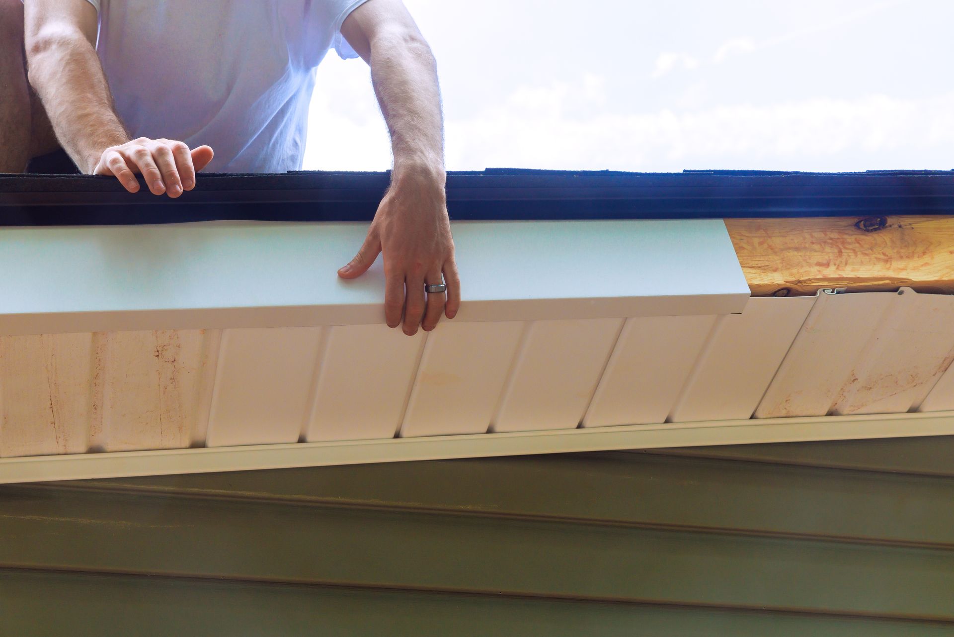 Personne installant un soffite blanc sous un avant-toit avec un revêtement vert.