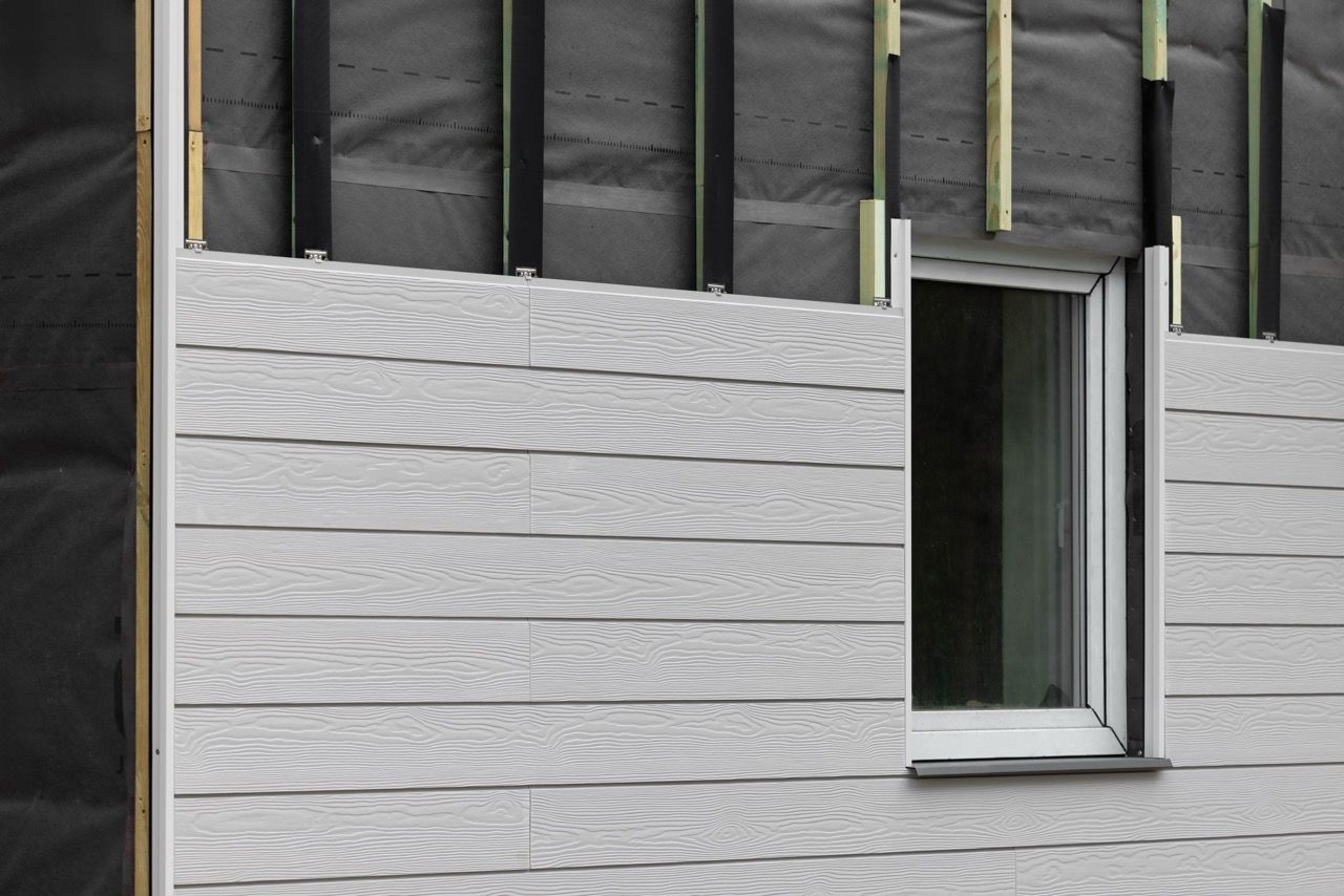 Un revêtement gris est installé autour d'une fenêtre blanche sur un bâtiment en construction.
