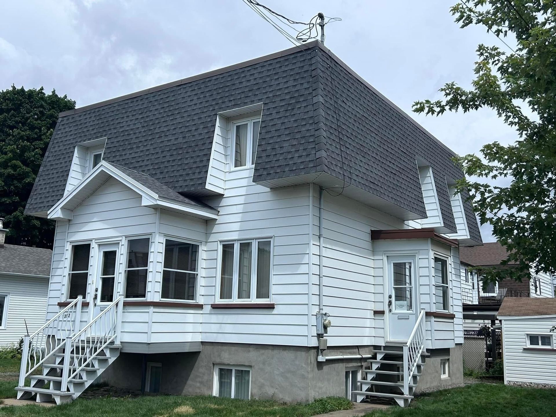 Maison blanche au toit gris foncé, avec plusieurs fenêtres et un escalier menant à la porte d'entrée.