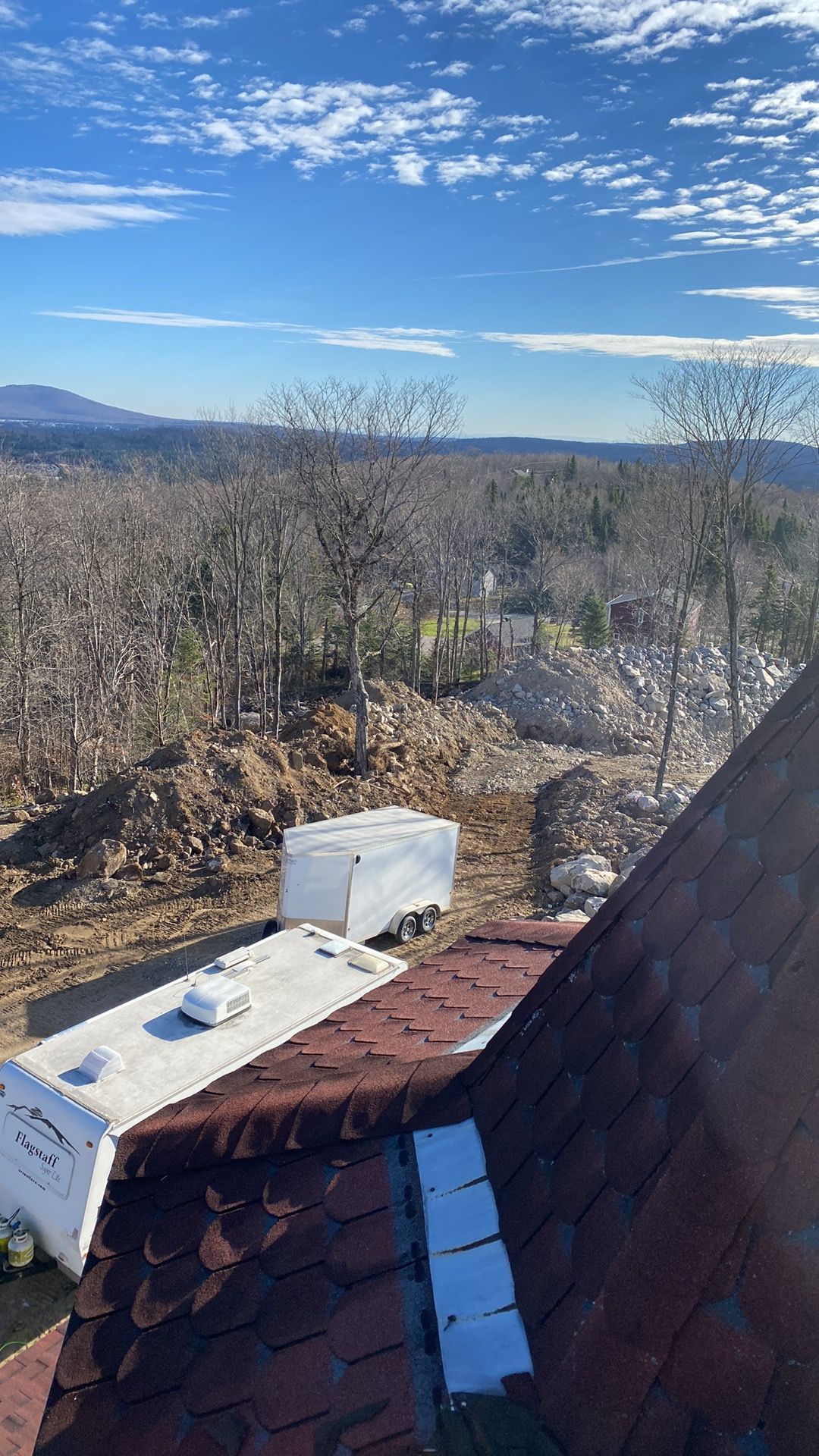 Vue depuis un bâtiment au toit rouge, montrant une forêt, un ciel bleu et une caravane blanche au sol.