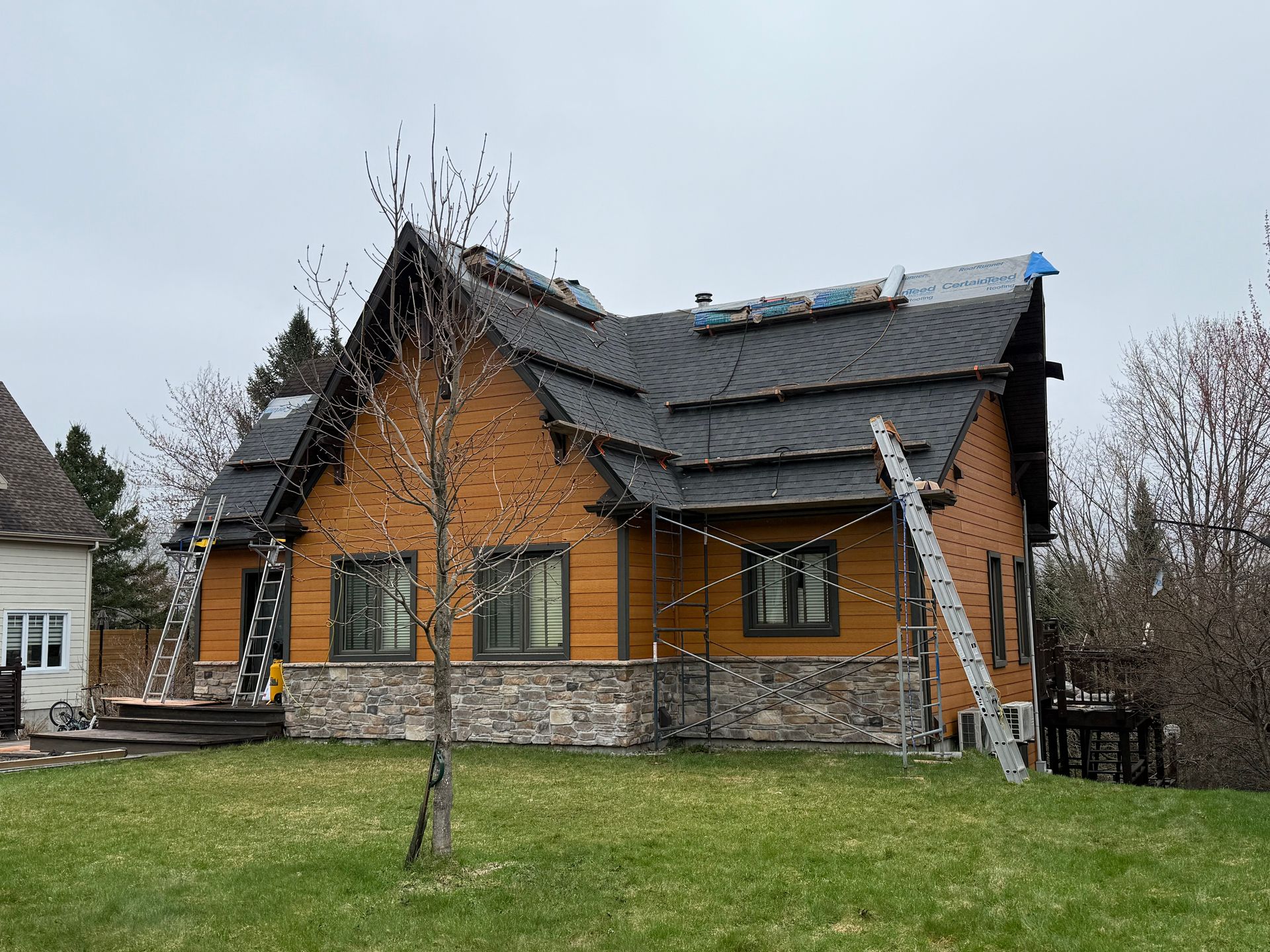 Maison avec un toit noir neuf et une façade en pierre ; des échelles sont appuyées contre la structure.