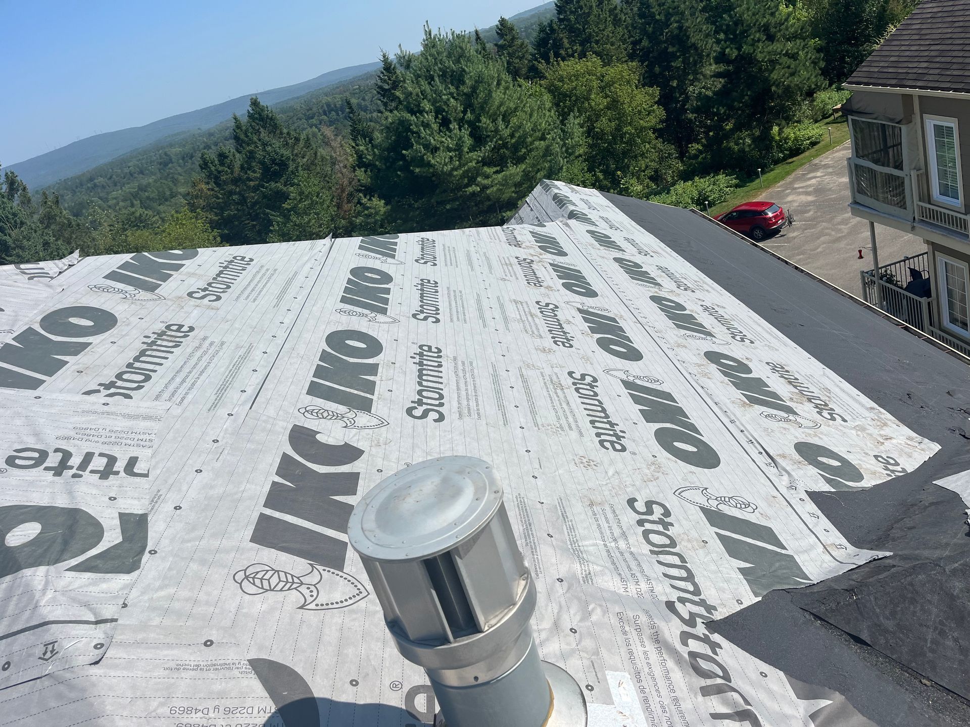 Toiture avec sous-couche protectrice, conduit de ventilation et vue sur la montagne boisée.