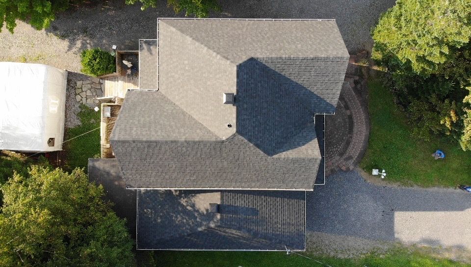 Vue aérienne d'une maison au toit gris foncé, entourée d'une allée et d'arbres.