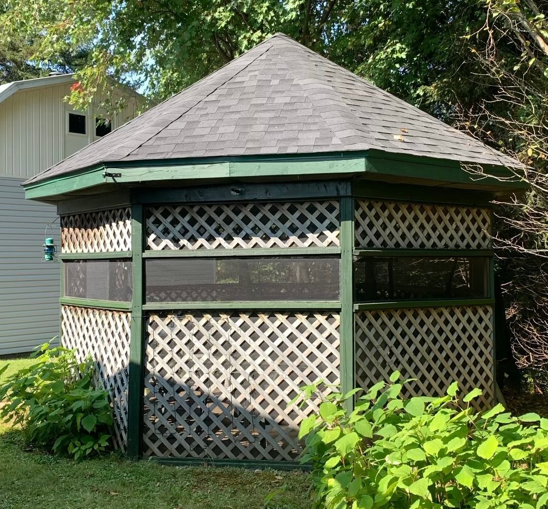Gazebo octogonal en bois avec des côtés en treillis et un toit gris foncé, dans une cour gazonnée.